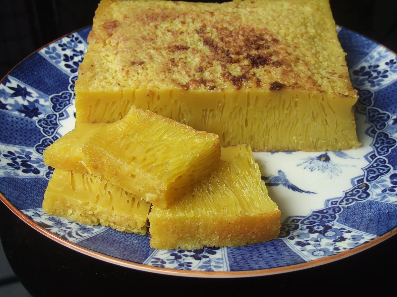 Slices of yellow bika ambon cake with a honeycomb texture on a blue and white plate
