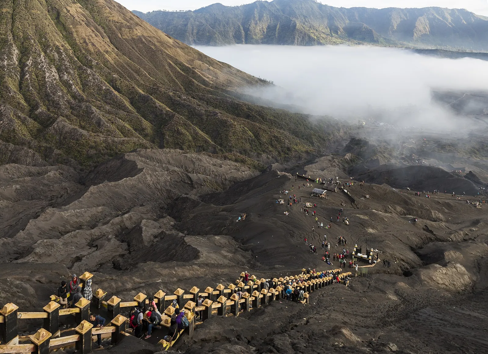 Visitors climbing the long concrete stairway up the ash slope to the rim of Bromo's crater, with morning mist in the caldera