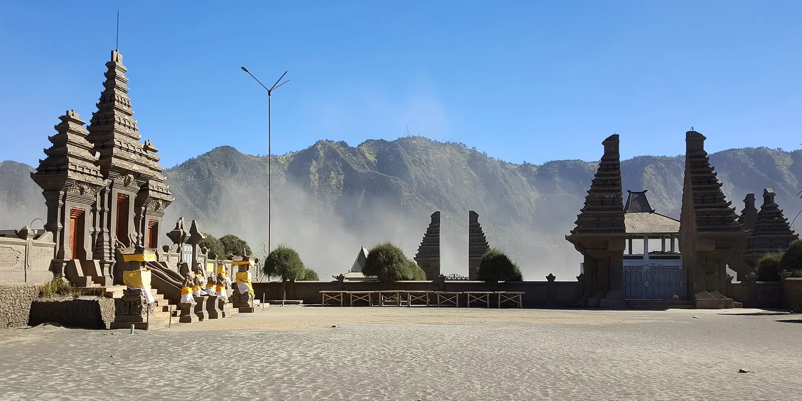 The carved stone gates and shrines of Pura Luhur Poten standing on the sand at the foot of the caldera wall under a blue sky