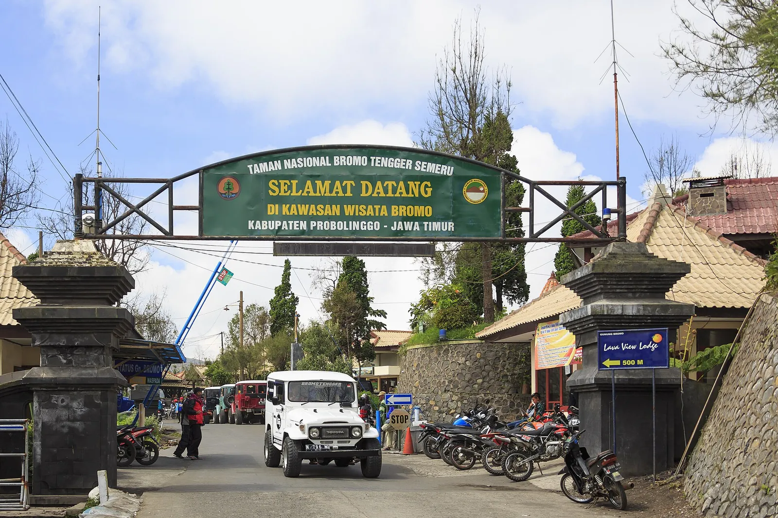 The 'Selamat Datang' arch over the road at the national park gate in Cemoro Lawang, with jeeps and motorbikes parked beside it