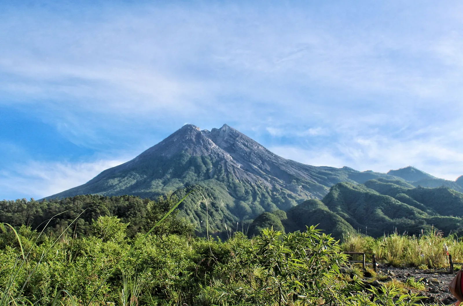 The green southern slopes of Mount Merapi rising to its grey summit under a blue sky