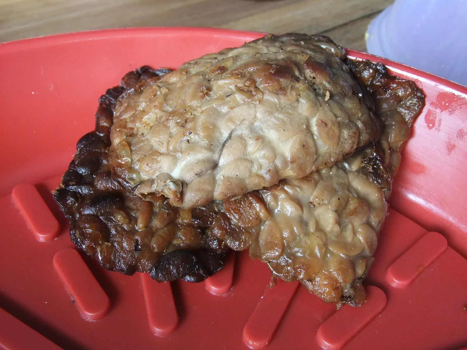 A piece of dark, glossy fried tempe bacem on a red plate