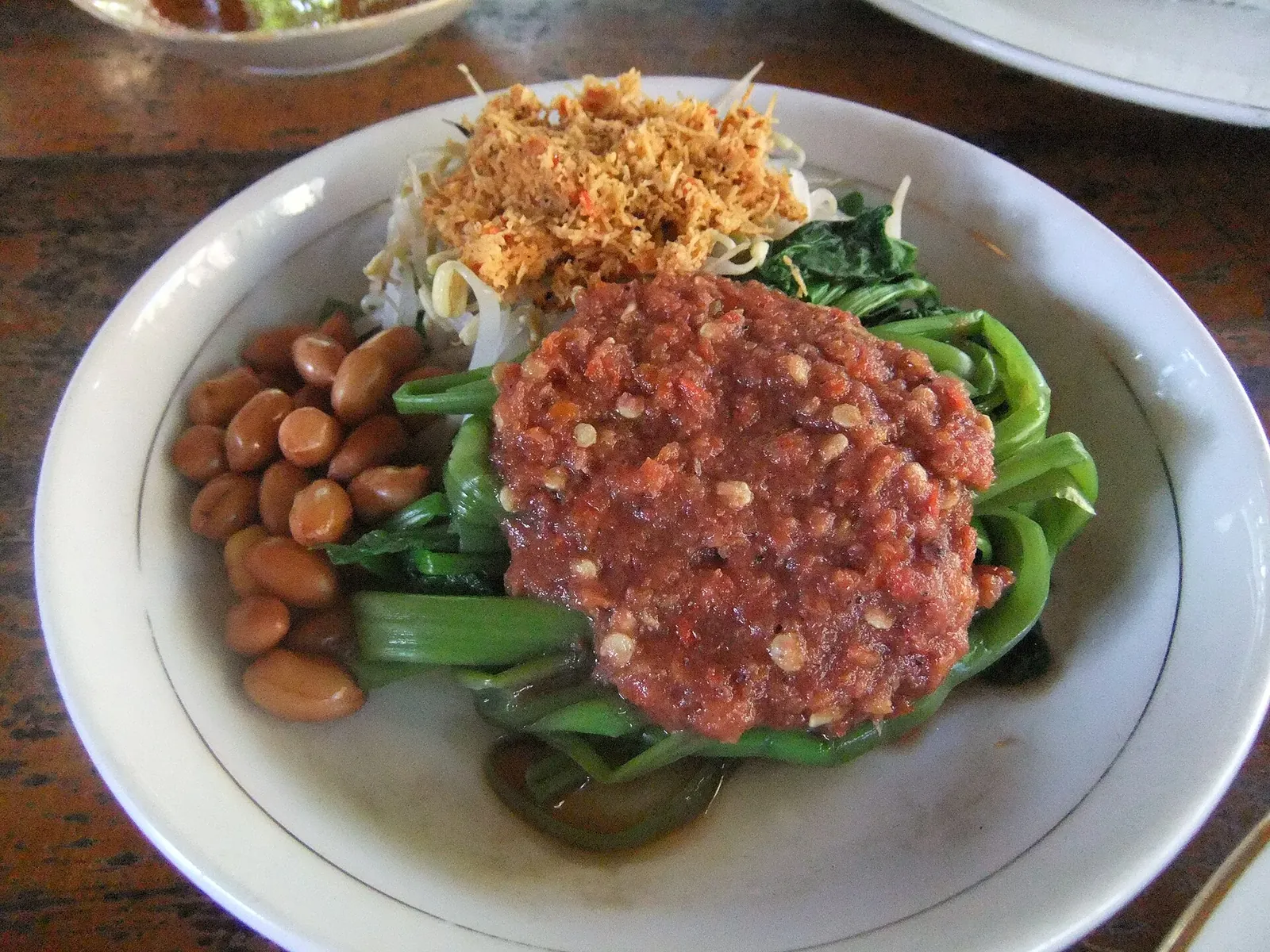 Plate of plecing kangkung: water spinach with red sambal, fried peanuts and grated coconut