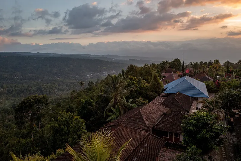Evening light over the forested valley below Munduk, with village roofs in the foreground