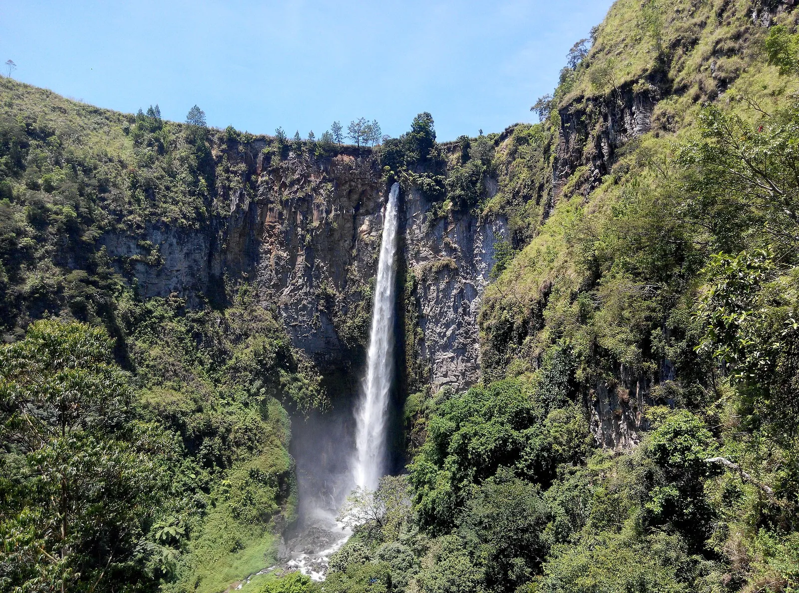 Sipiso-piso waterfall dropping in a long thin stream down a forested cliff into a gorge