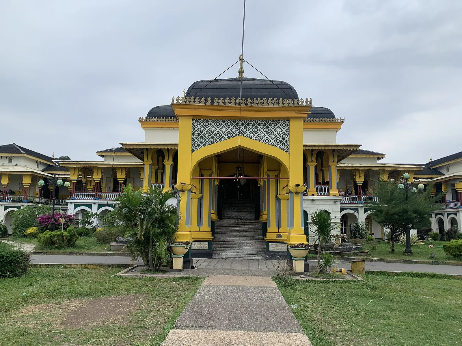 The yellow facade and central entrance of Maimun Palace in Medan, with a path across the lawn