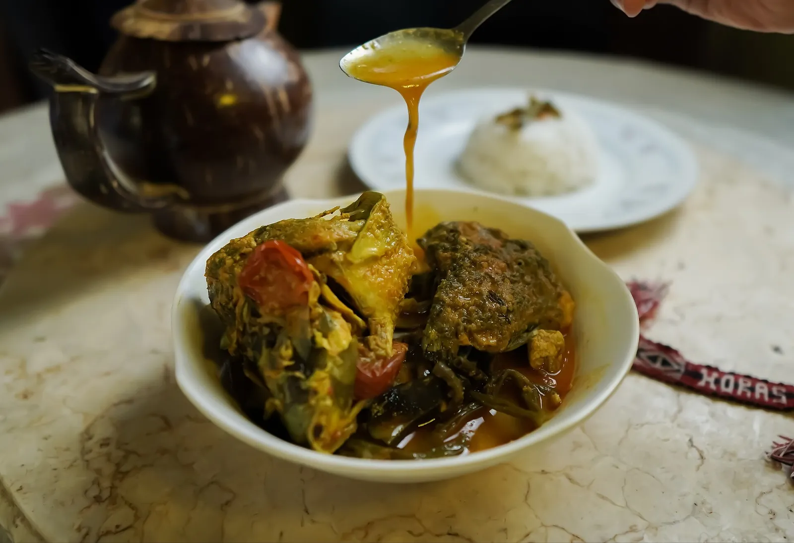 A bowl of Batak arsik fish in a yellow spiced sauce, with rice on the side and sauce being spooned over