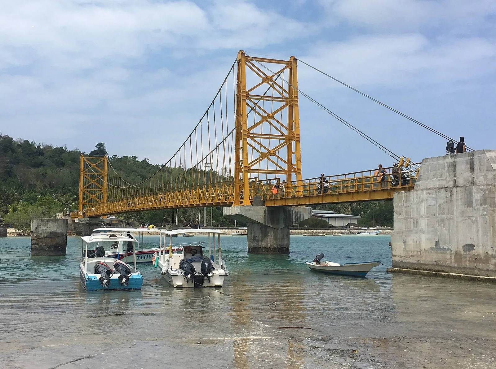 Yellow suspension bridge between Nusa Lembongan and Nusa Ceningan above boats in the channel