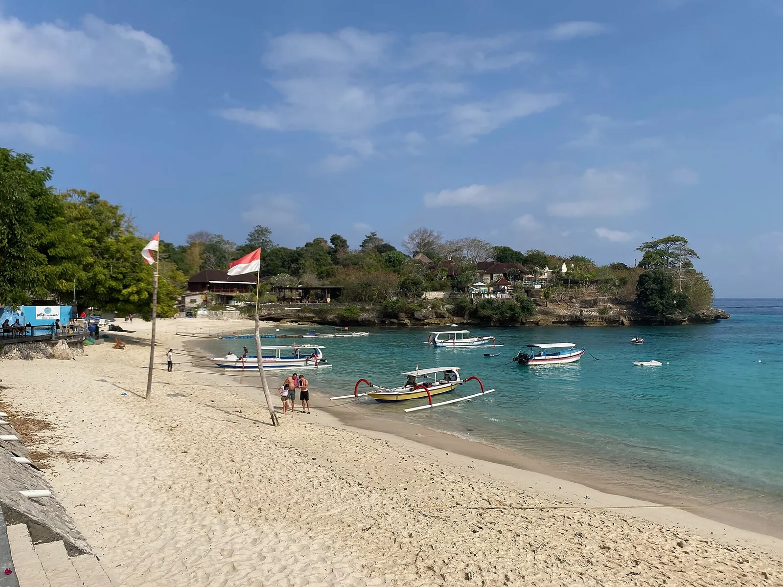 Sandy beach at Mushroom Bay with outrigger boats and an Indonesian flag