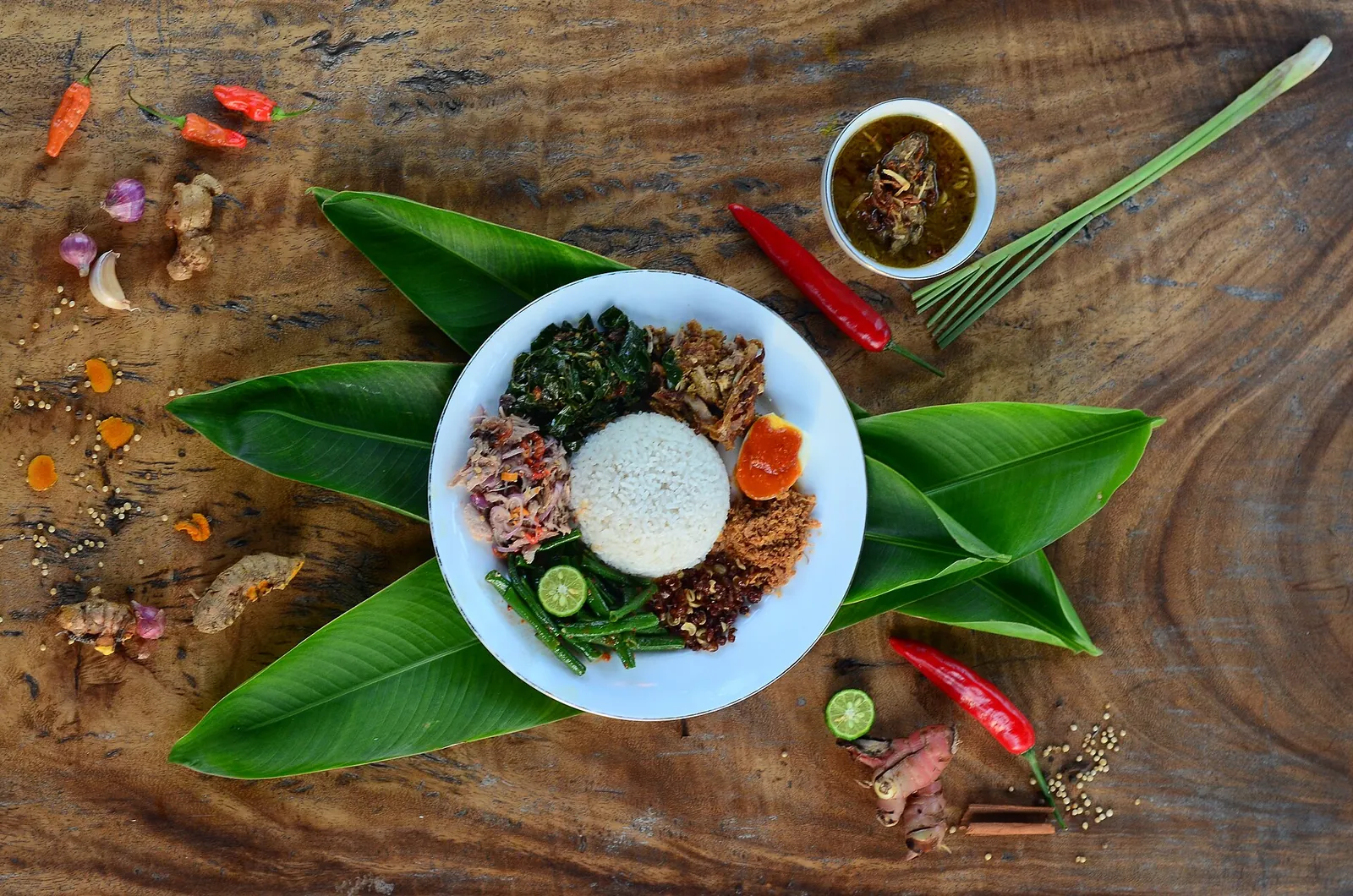 Plate of Balinese nasi campur with rice, vegetables, meats and sambal on banana leaves