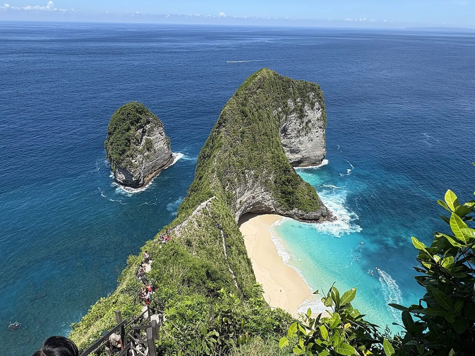 Kelingking Beach on Nusa Penida seen from the clifftop, a green headland above a curve of white sand and turquoise sea