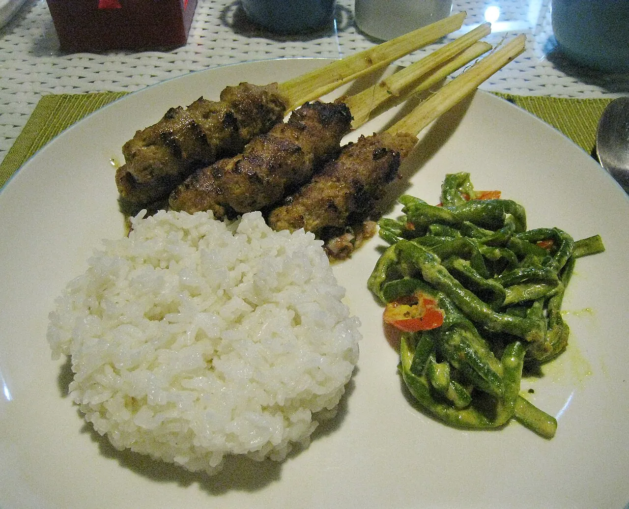 Sate lilit, minced pork satay on sticks, served with rice and spiced long beans on a plate