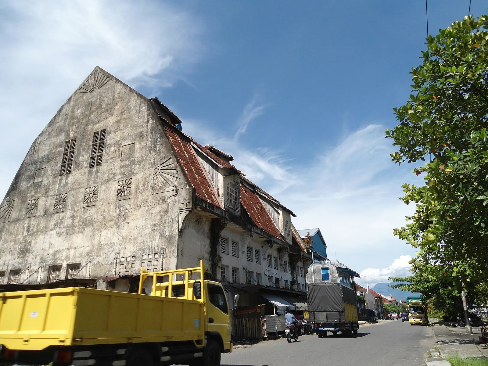 An old gabled warehouse with weathered walls on Jalan Batang Arau in Padang, with a truck parked in front