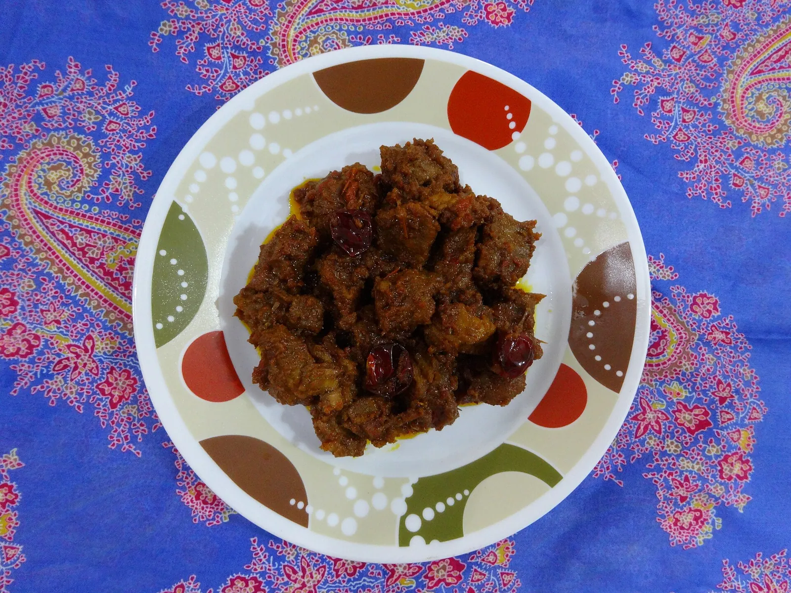 A plate of dark, dry beef rendang on a patterned cloth