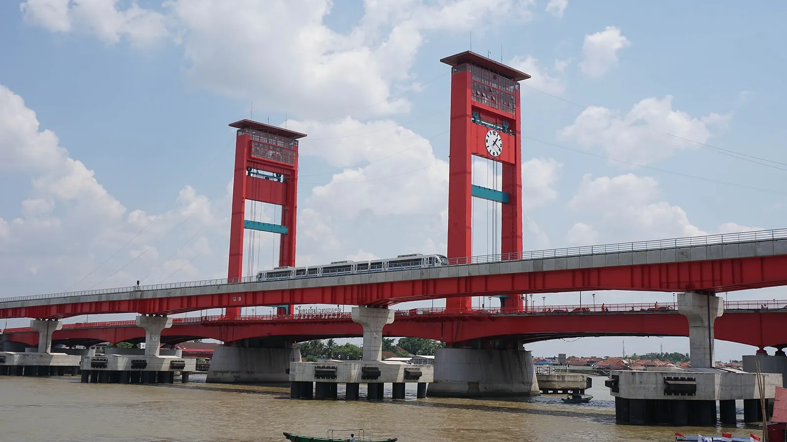 The red towers of the Ampera Bridge over the brown Musi River in Palembang, with the LRT viaduct running alongside