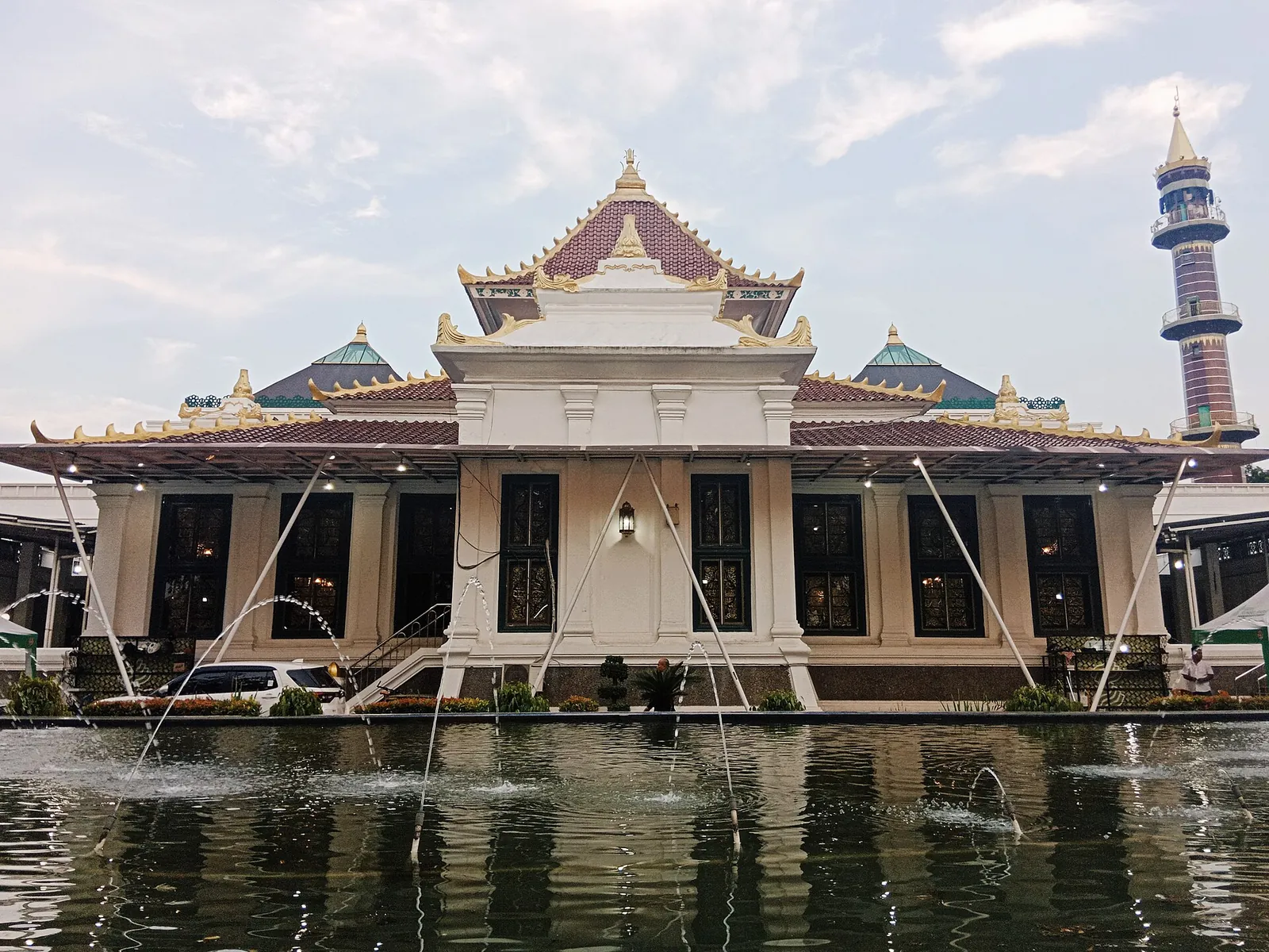 The tiered roof and white prayer hall of the Great Mosque of Palembang with its minaret, reflected in a pool