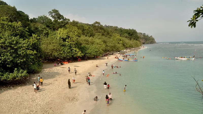 Swimmers and families on a pale-sand beach below the forested headland at Pangandaran