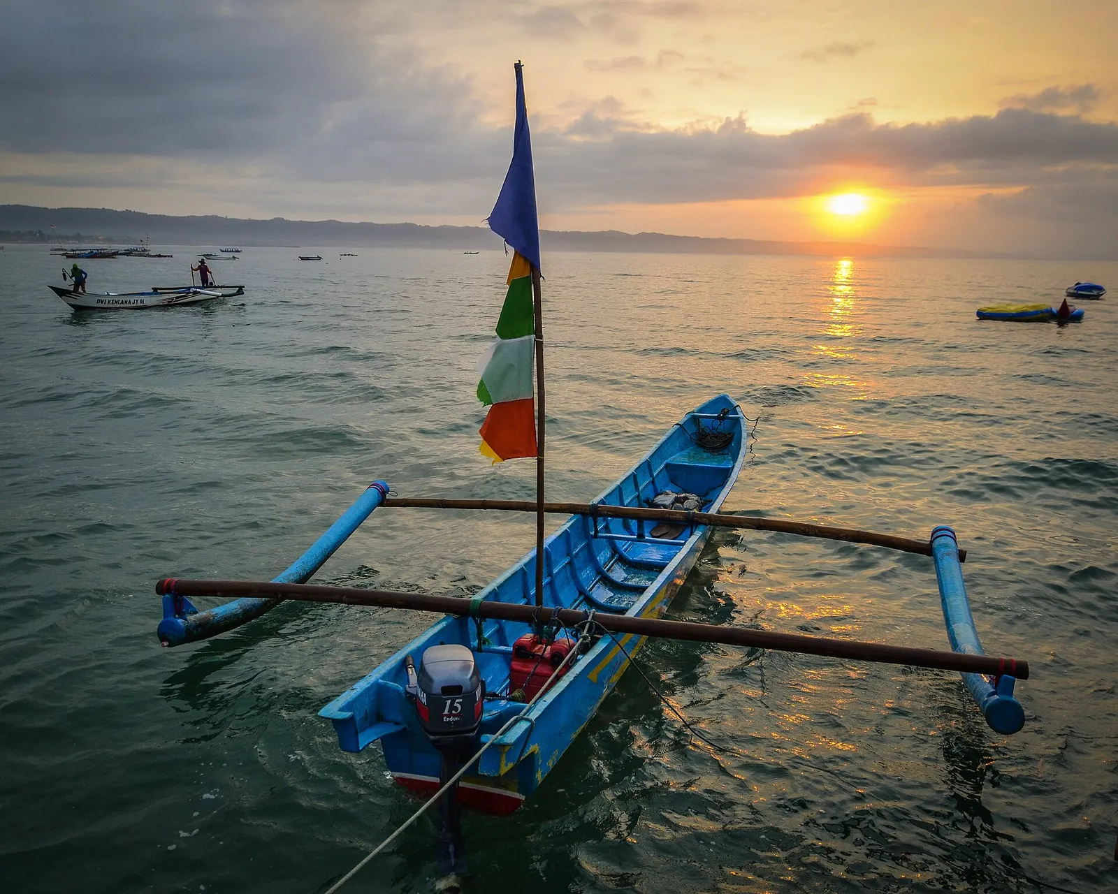 A blue outrigger fishing boat moored in calm water at sunrise off Pangandaran's East Beach
