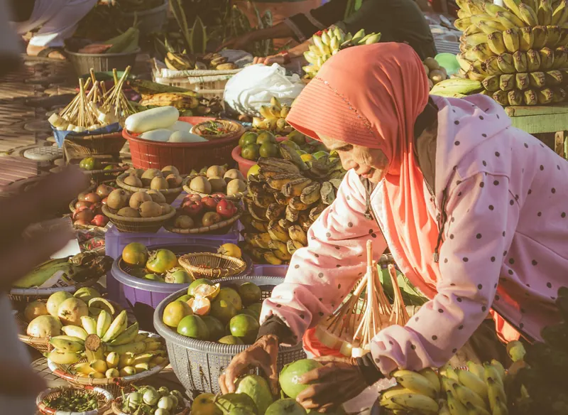 A fruit seller in a pink headscarf arranging bananas, mangosteens and other fruit in baskets at the Banjarmasin floating market