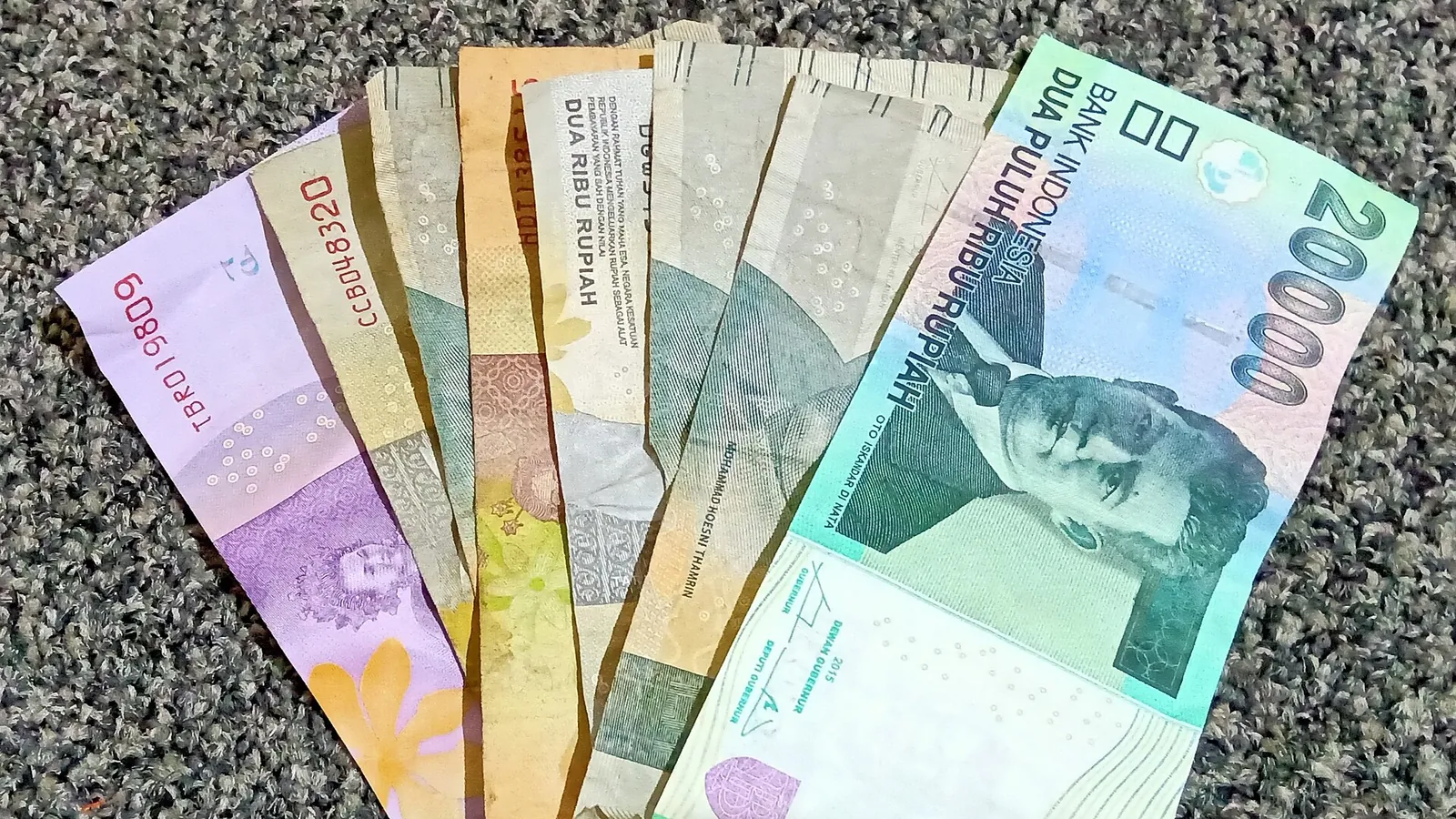A fan of Indonesian rupiah banknotes from 2,000 to 20,000 rupiah on a grey surface