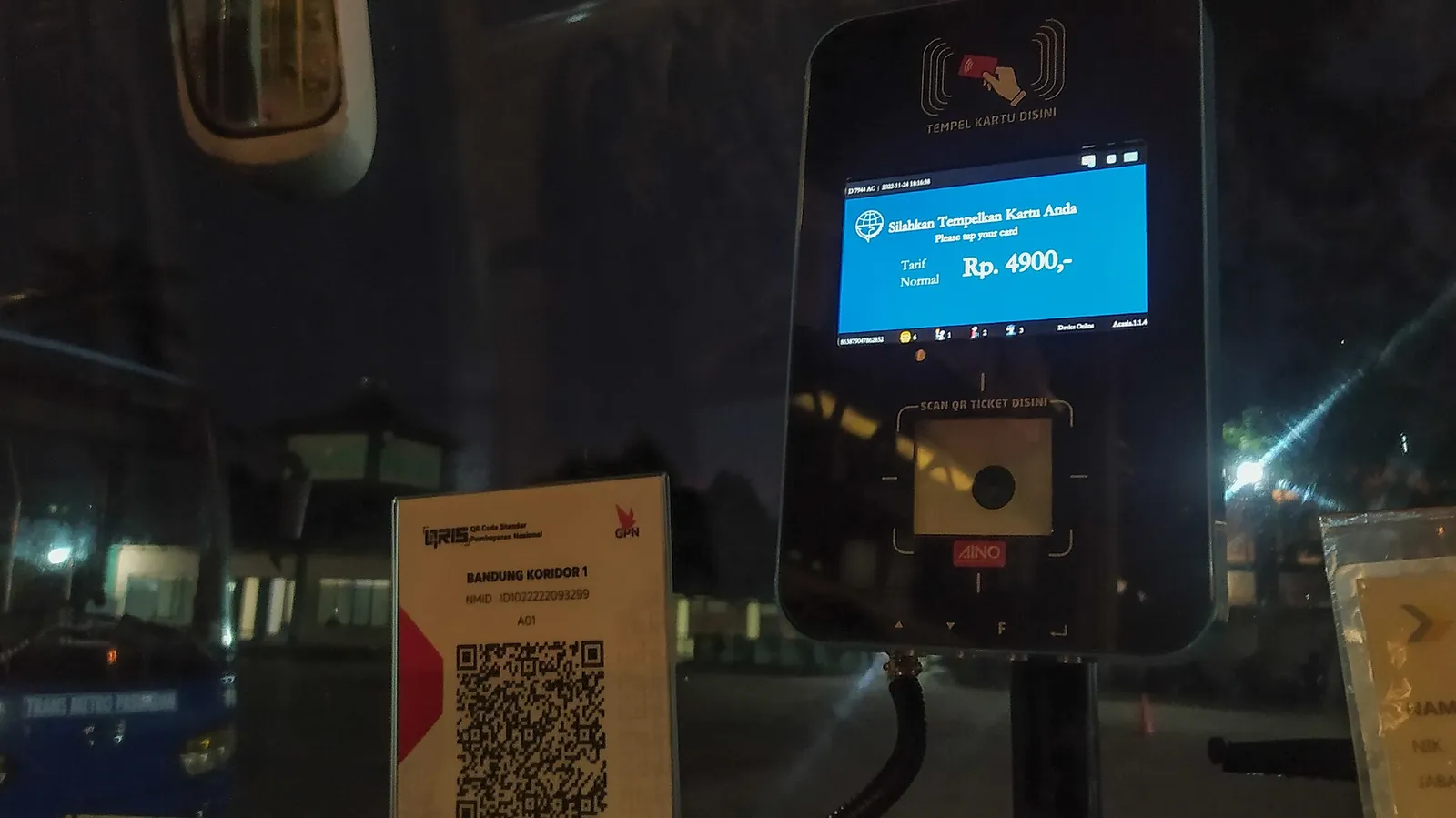 A card tap reader and a printed QRIS code mounted beside the door inside a Trans Metro Pasundan bus
