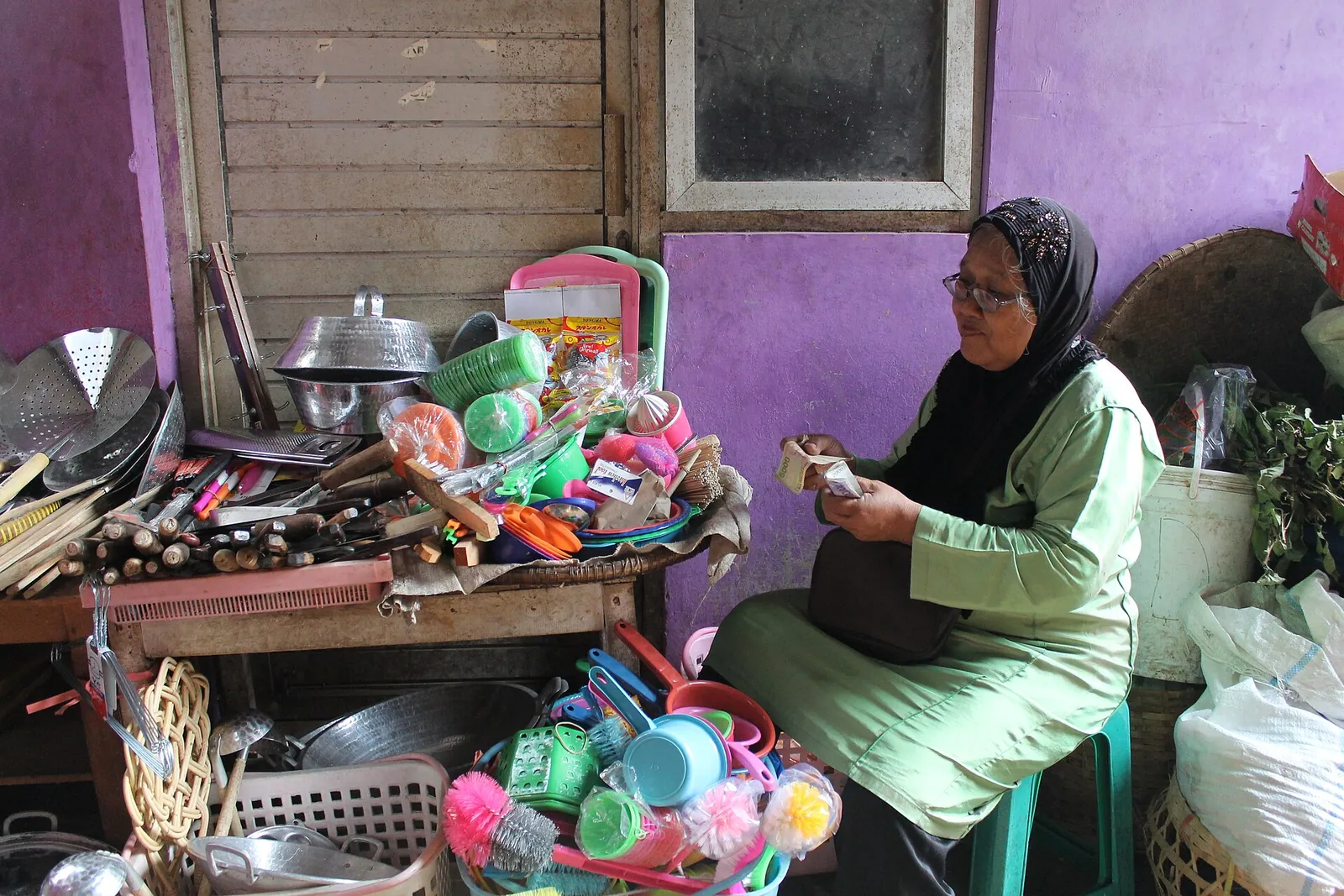 A market trader in a green headscarf counting banknotes among household goods at her stall