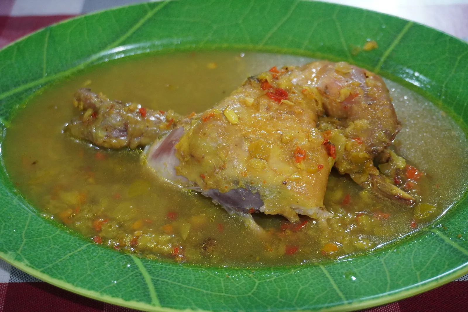 A plate of ayam betutu, spiced chicken in a yellow chilli-flecked sauce, on a green plate