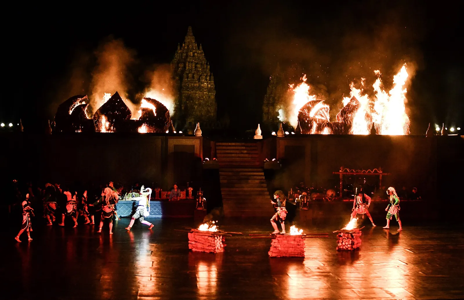 Ramayana ballet dancers on an open-air stage at night with fire and a lit temple behind
