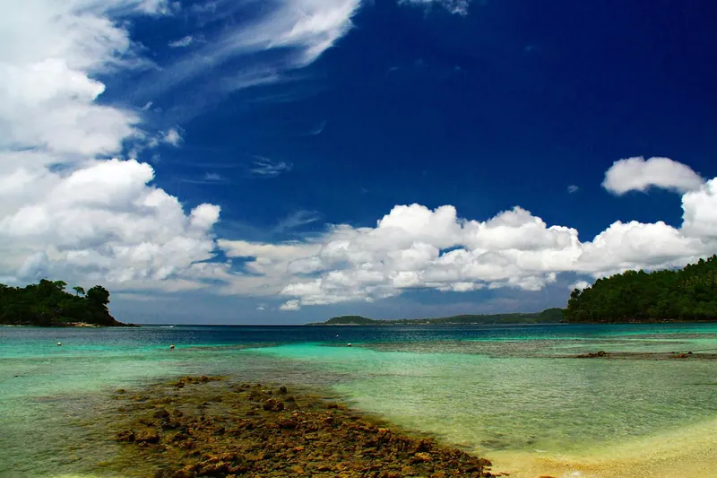 Clear turquoise shallows over a rocky reef flat at Iboih beach on Pulau Weh, with forested headlands under a blue sky