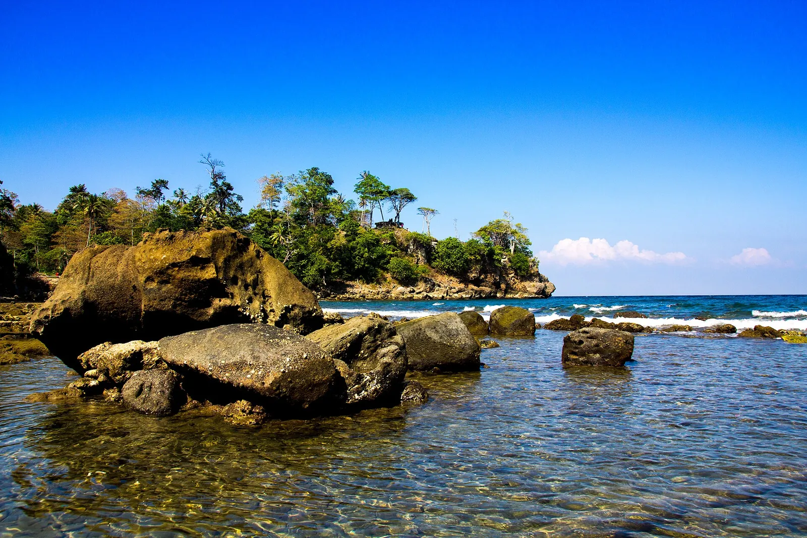 Rocks and clear water at the black-sand Anoi Itam beach on Pulau Weh, under a blue sky