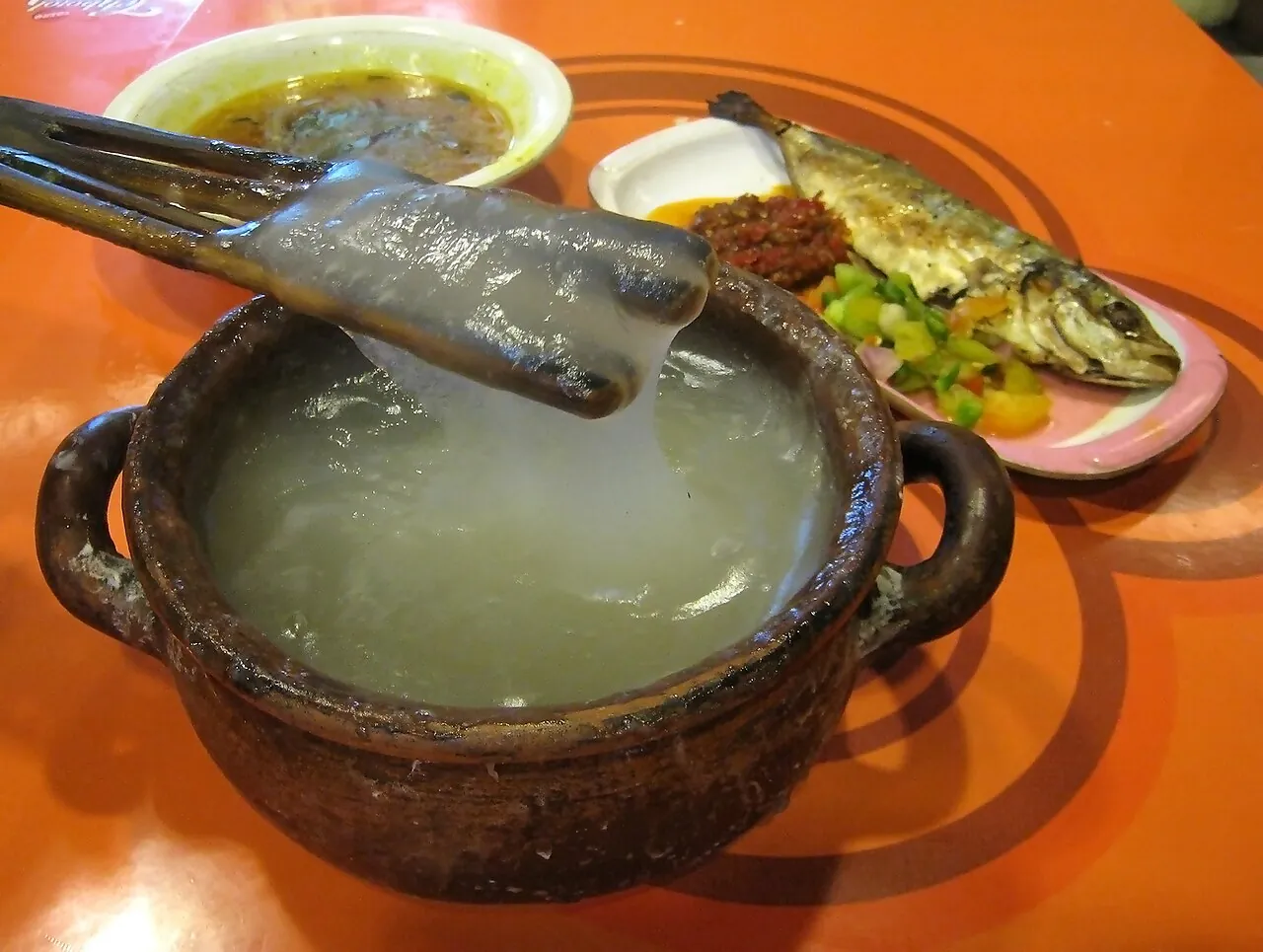Papeda sago congee in a clay pot with yellow fish soup and a grilled fish with sambal