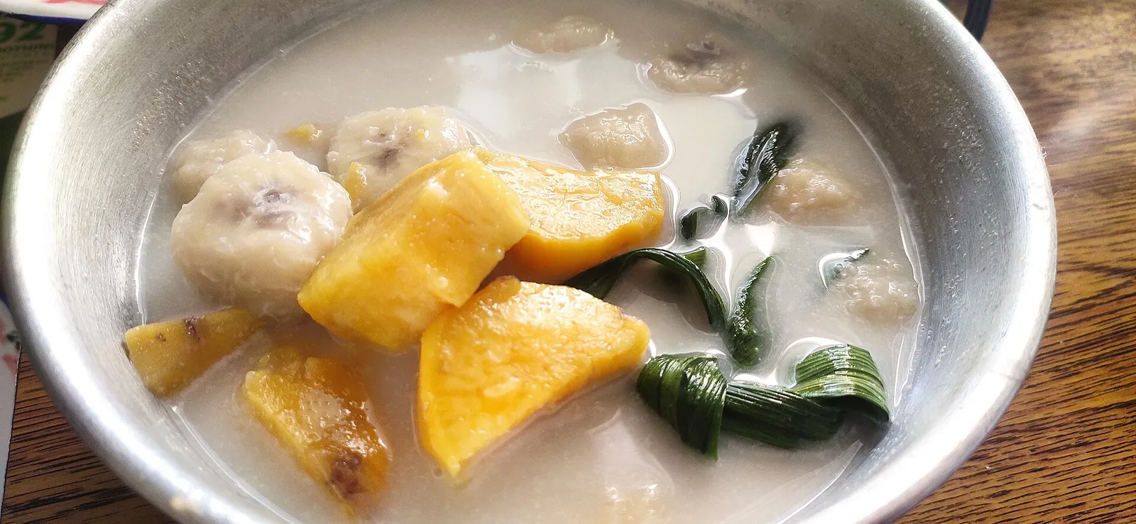 A bowl of kolak with chunks of banana and orange sweet potato in coconut milk with pandan leaves