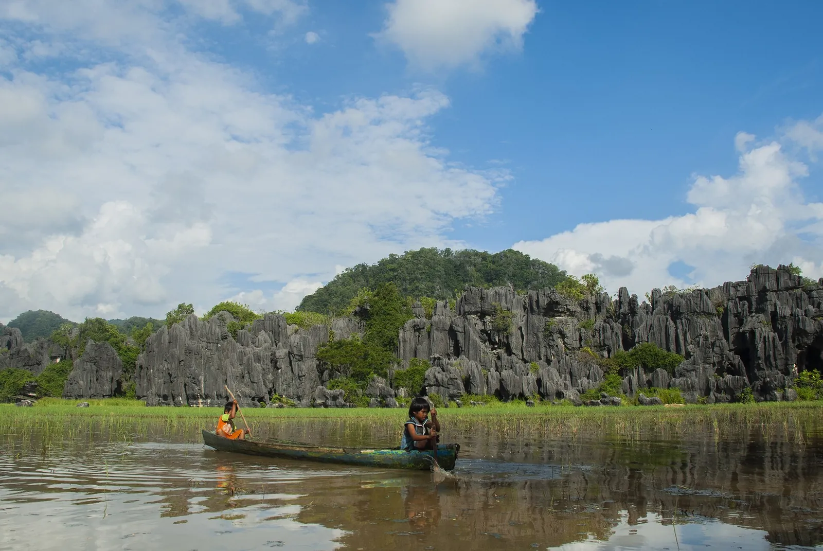 A wooden boat on the river at Rammang-Rammang below a wall of jagged limestone karst