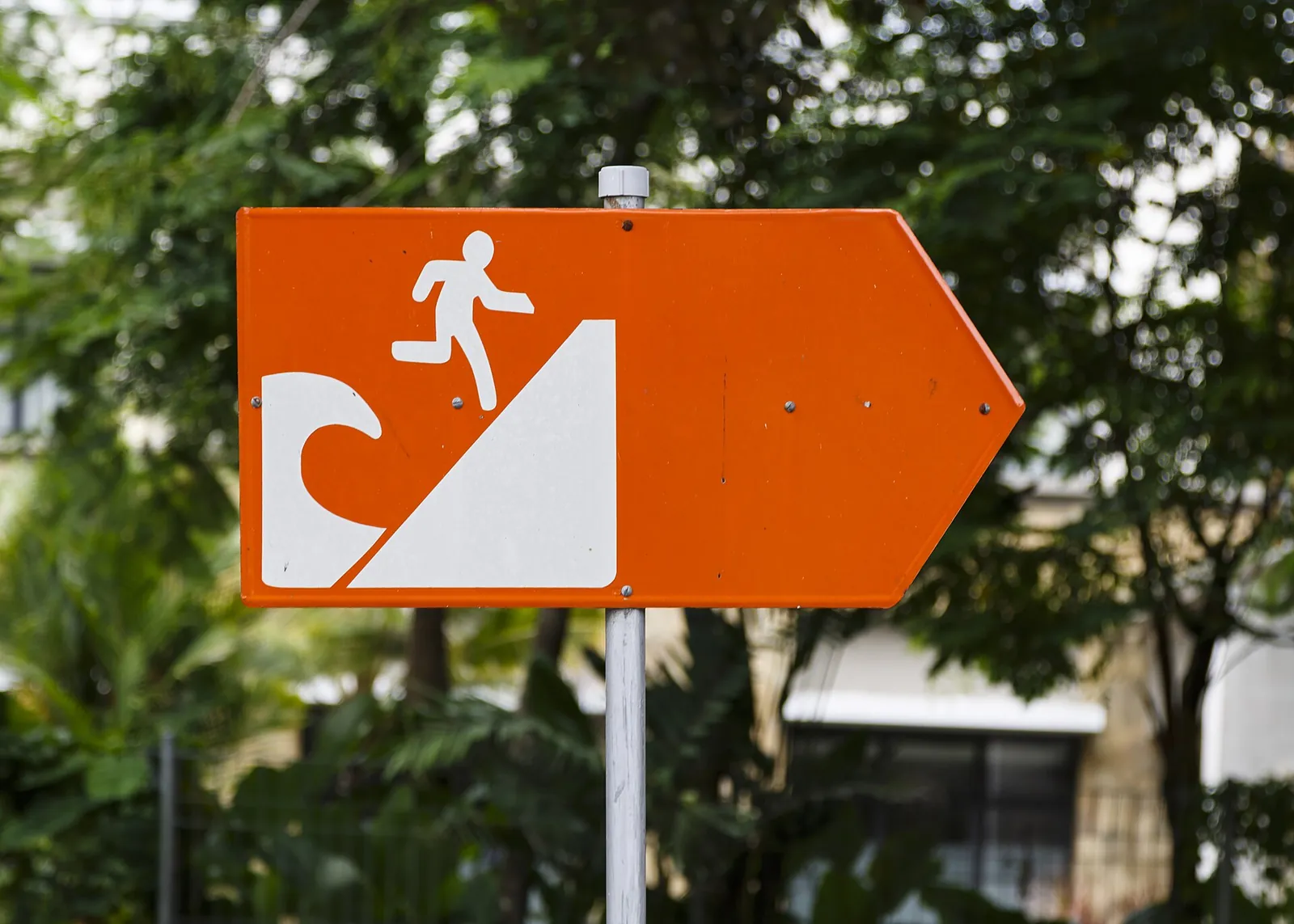 Orange tsunami evacuation route sign with a running figure and a wave in Nusa Dua, Bali