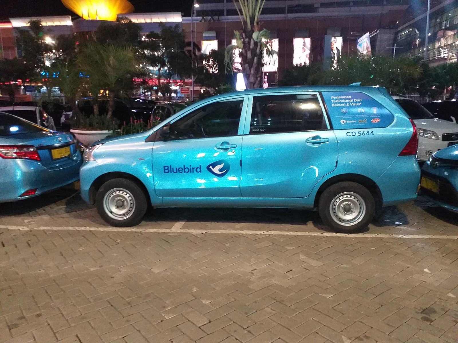 A light-blue Bluebird taxi parked outside Pondok Indah Mall in Jakarta at night