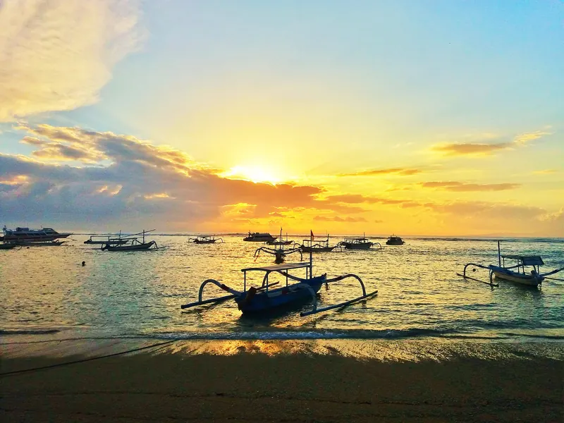 Sunrise over Sanur Beach with traditional jukung outrigger boats moored in the calm water