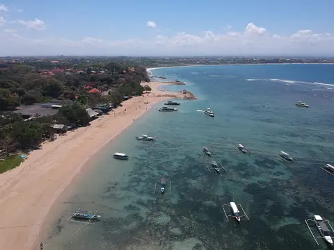 Aerial view of Sanur's coastline with a sandy beach, low-rise hotels among trees and boats moored over the reef lagoon