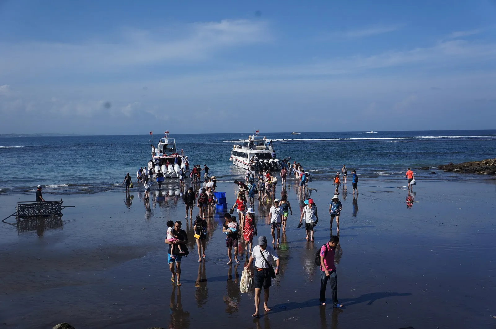 Travellers wading ashore at Sanur Beach from fast boats anchored in the shallows