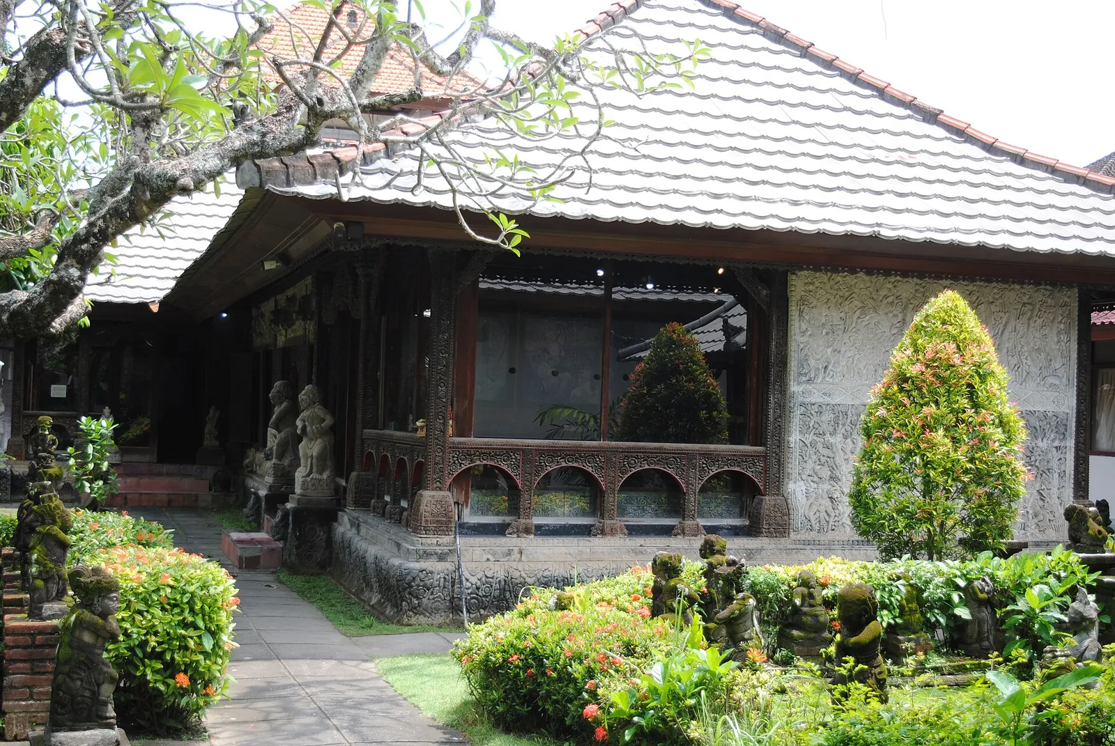 A traditional Balinese house with a tiled roof, stone statues and a garden at the Museum Le Mayeur in Sanur