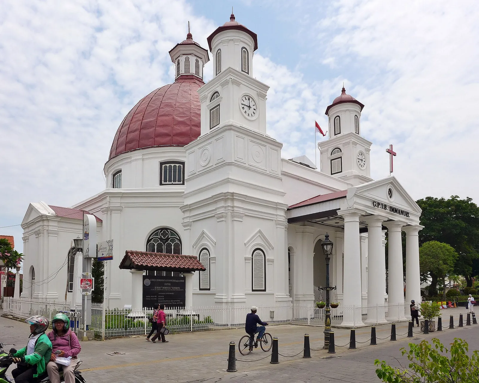 White Blenduk Church with its red copper dome and twin clock towers in Semarang's Old Town, with a cyclist passing in front
