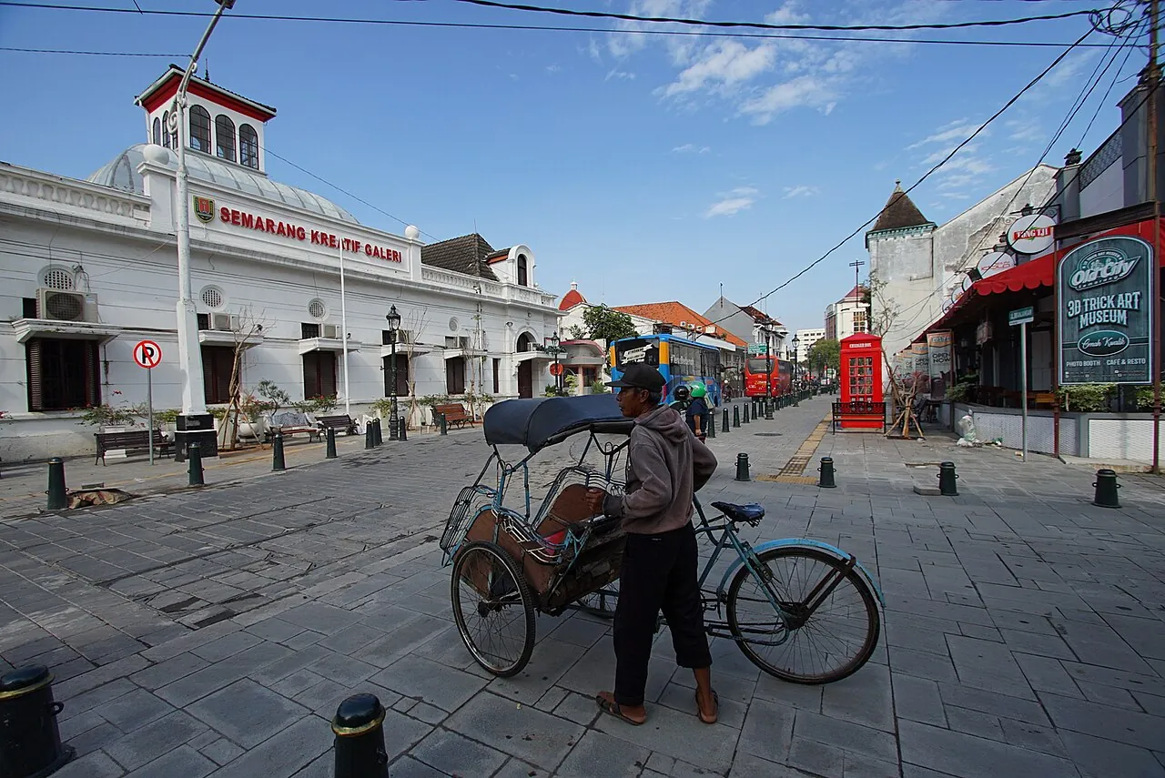 A becak driver with his trishaw on a paved street lined with colonial buildings in Kota Lama, Semarang