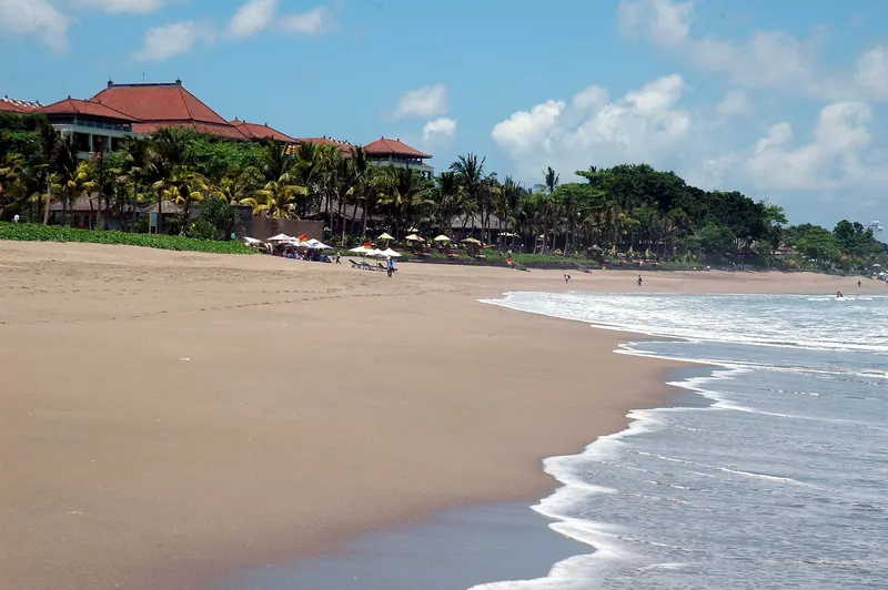 Wide sandy beach with breaking surf and a palm-fringed resort behind it at Petitenget, Seminyak