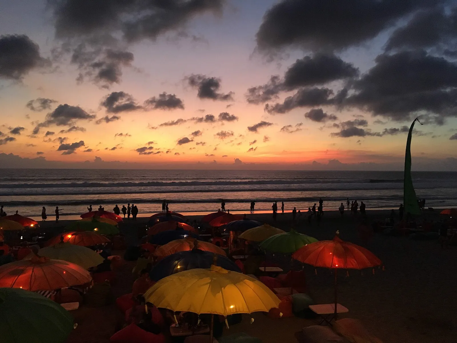 Beach umbrellas and a tall decorative pole silhouetted against an orange sunset on Seminyak Beach