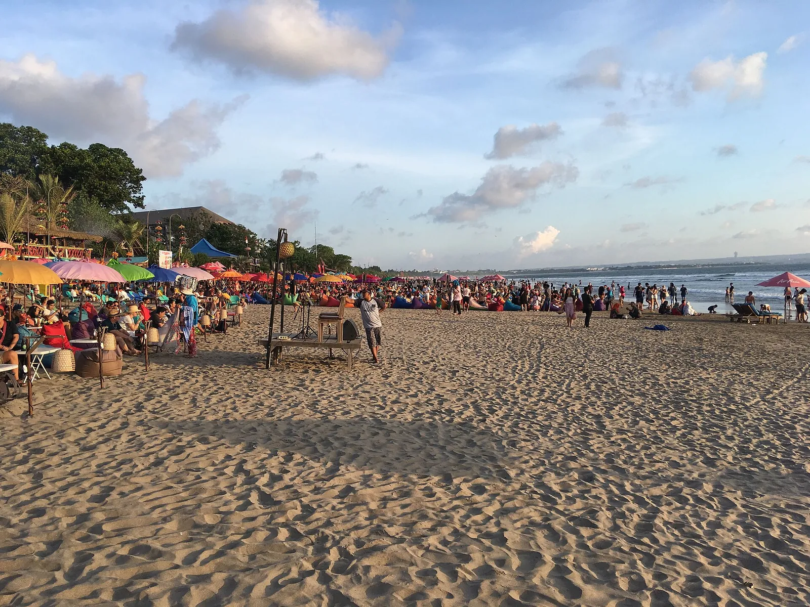 Crowded sand with colourful umbrellas and beach stalls under a blue sky on Seminyak Beach