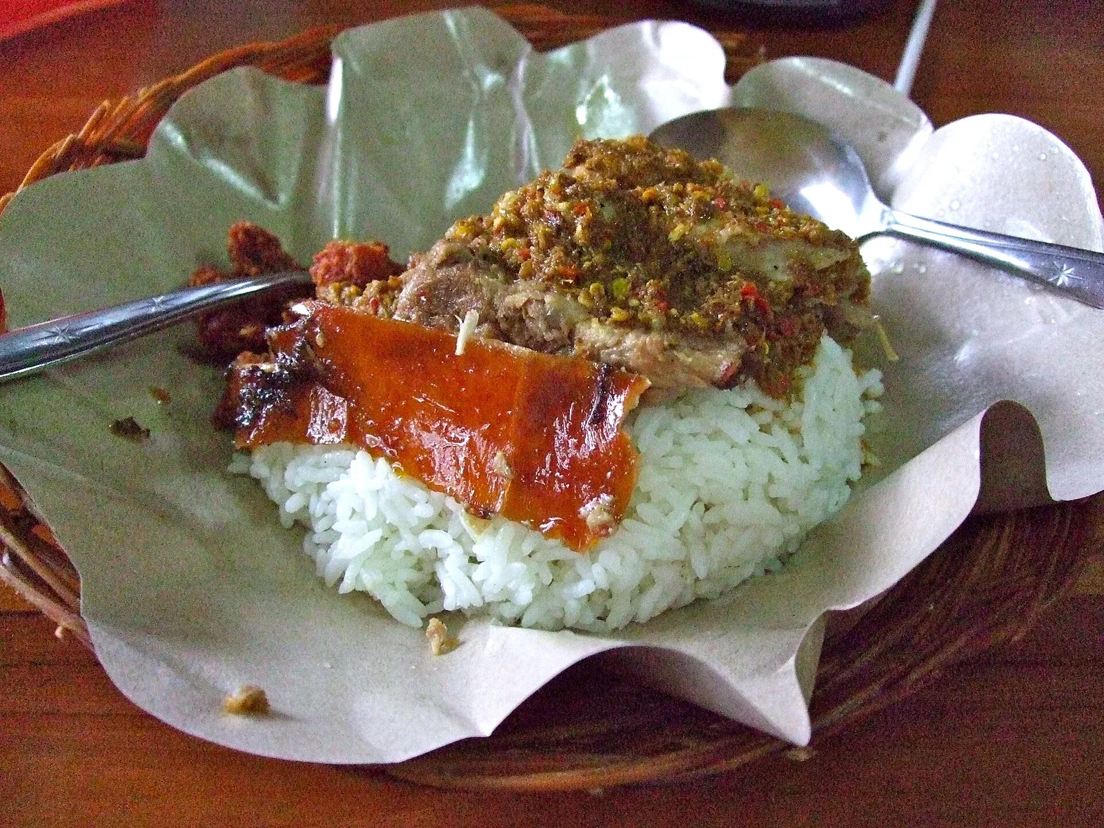 Plate of babi guling with crackling, spiced pork and sambal on rice served on paper