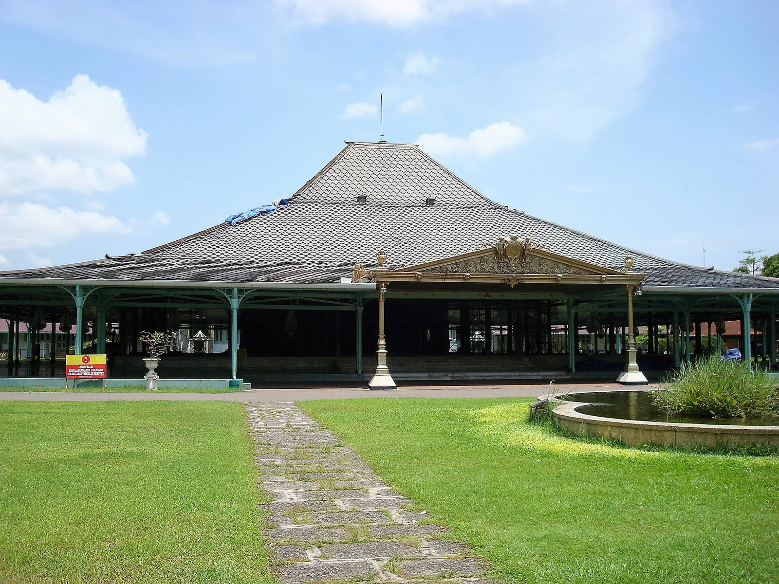 The great timber pendopo of the Pura Mangkunegaran in Solo under a blue sky, with a lawn and path in front