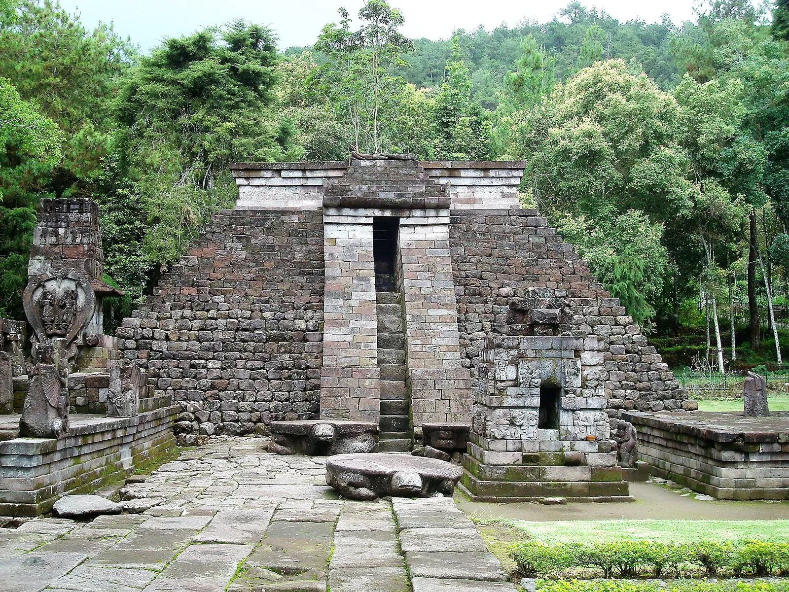 The stepped stone pyramid of Candi Sukuh on Mount Lawu, with carved statues in the forested courtyard