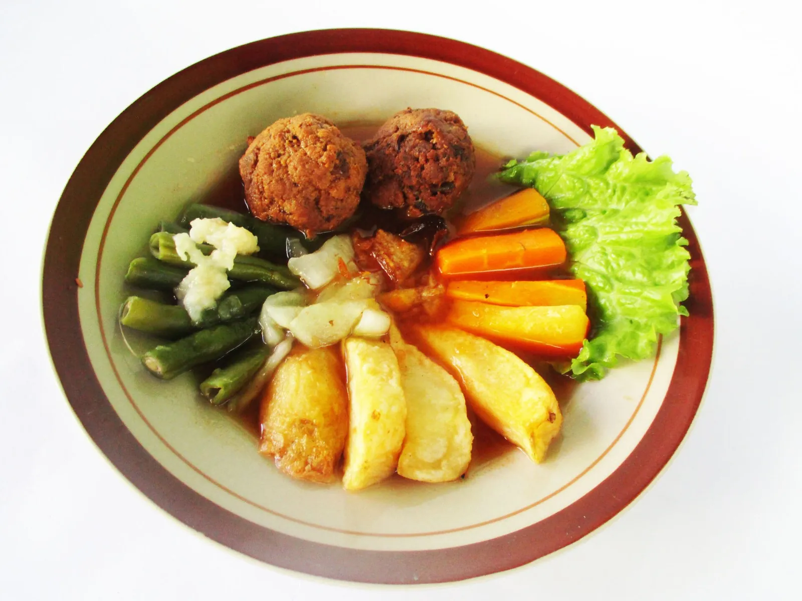 A plate of Selat Solo with two round meat patties, fried potatoes, carrots, green beans and lettuce in a thin brown sauce