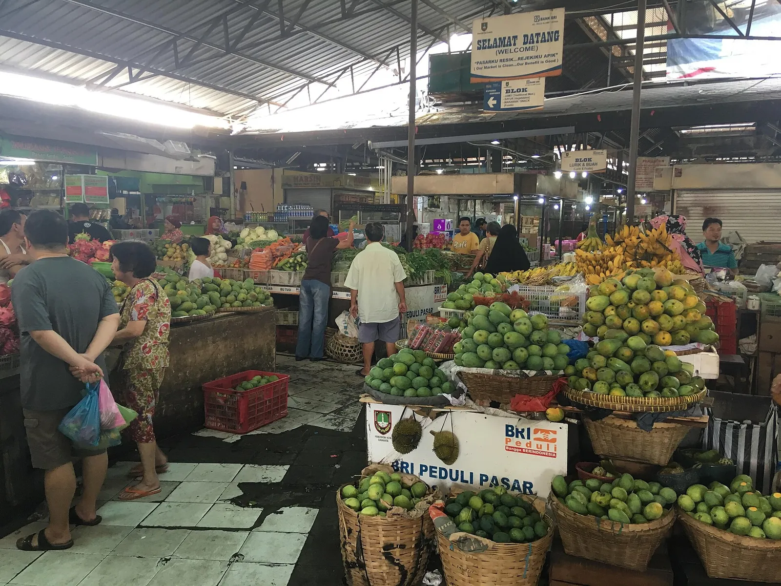 Baskets and piles of mangoes and bananas at fruit stalls under the roof of Pasar Gede in Solo