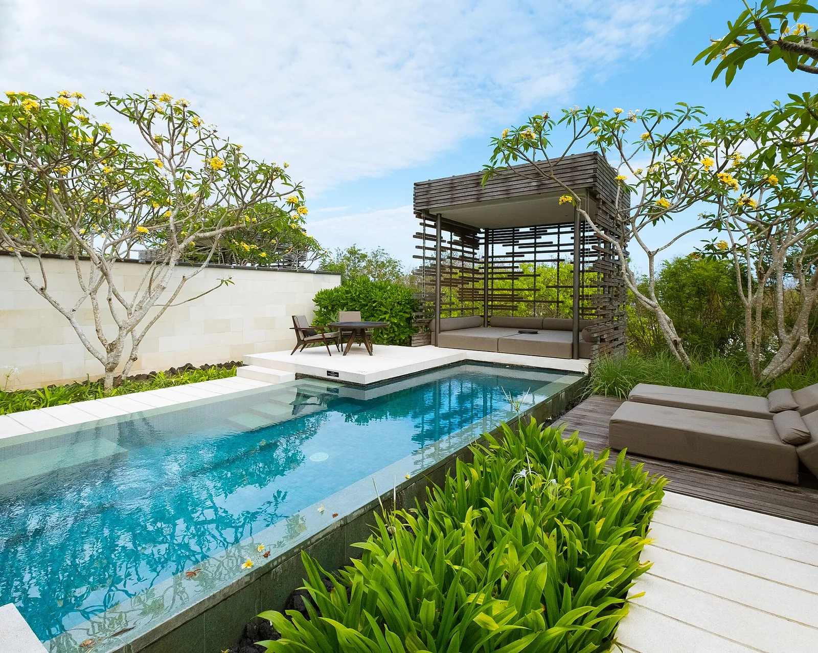 Long swimming pool beside a wooden pavilion and frangipani trees at Alila Villas in Bali